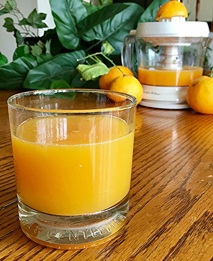 a glass filled with orange juice sitting on top of a wooden table