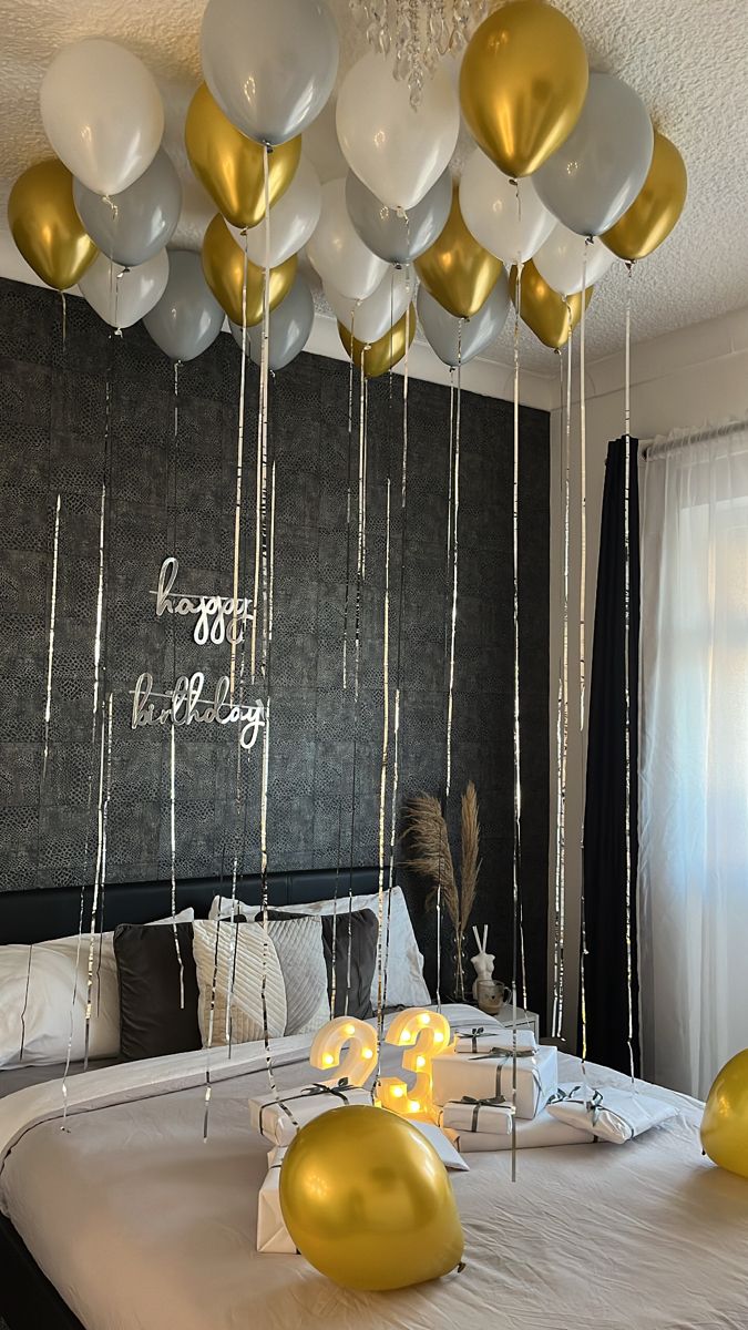 white and gold balloons are hanging from the ceiling above a bed in a room with black walls