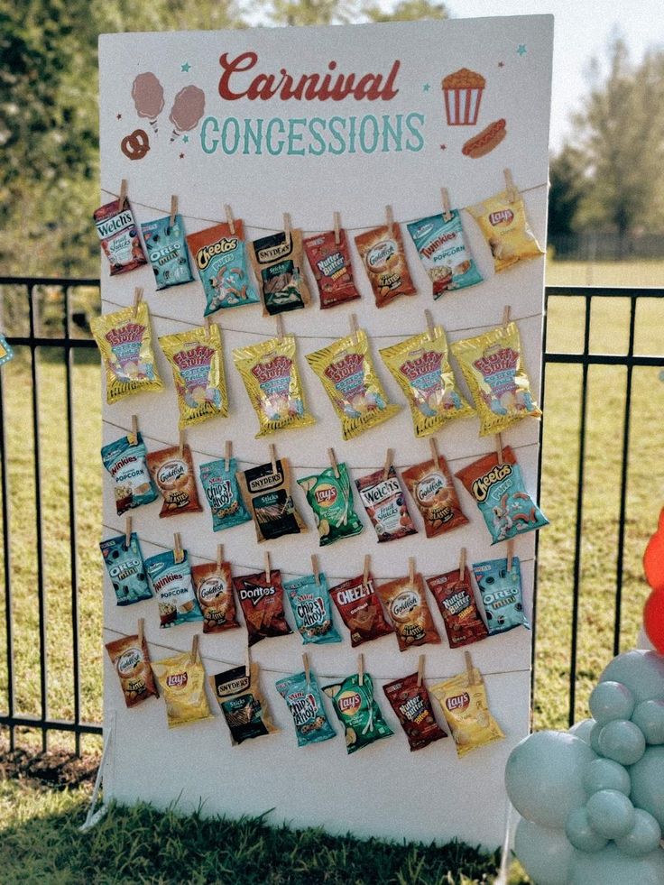 a sign that is on the grass with balloons in front of it and some candies hanging from clothes pins