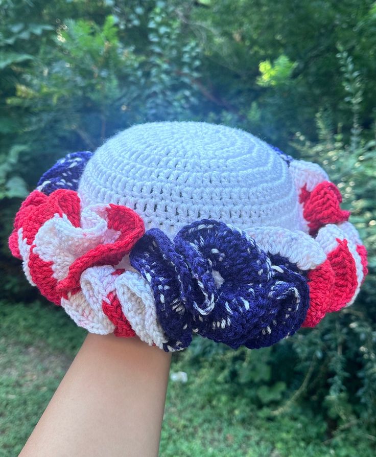 a woman's hand wearing a crocheted hat with red, white and blue flowers