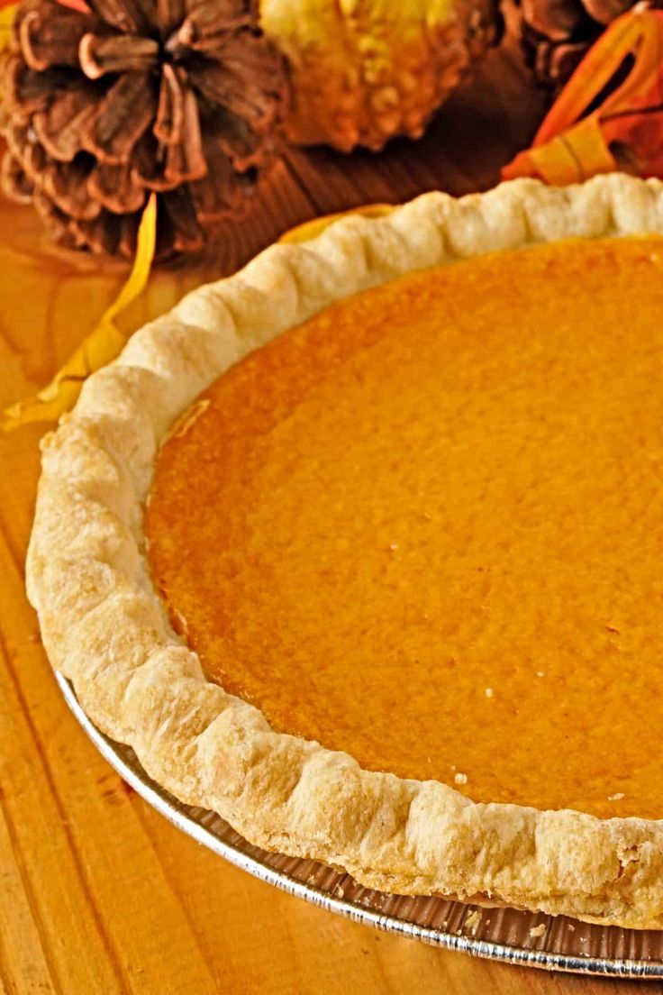 a pie sitting on top of a wooden table next to autumn leaves and pumpkins