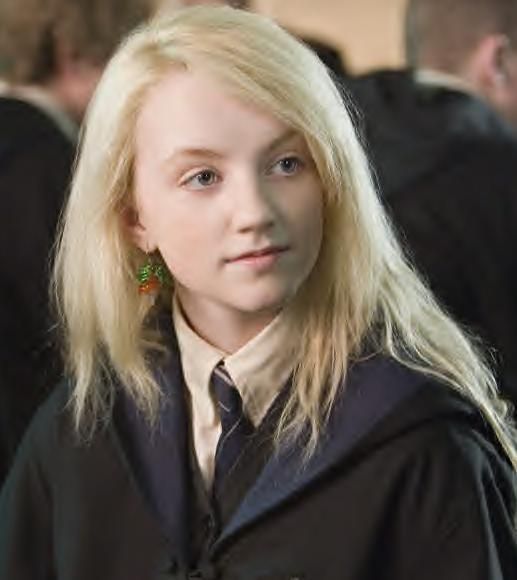 a girl with blonde hair wearing a harry potter robe and green brooches is standing in front of other people