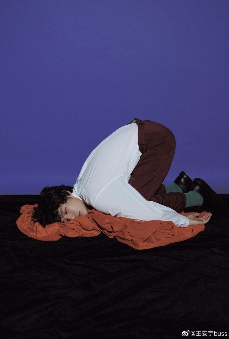 a person laying on top of a bed with an orange blanket and black shoes in front of a blue wall