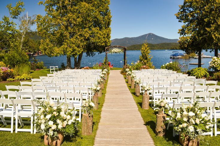 an outdoor wedding venue with white chairs and flowers on the aisle leading to the water