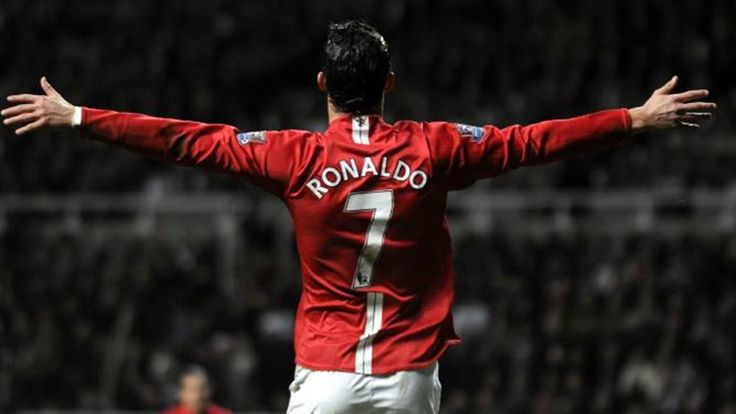 a man with his arms outstretched in the air on a soccer field, wearing a red shirt and white shorts