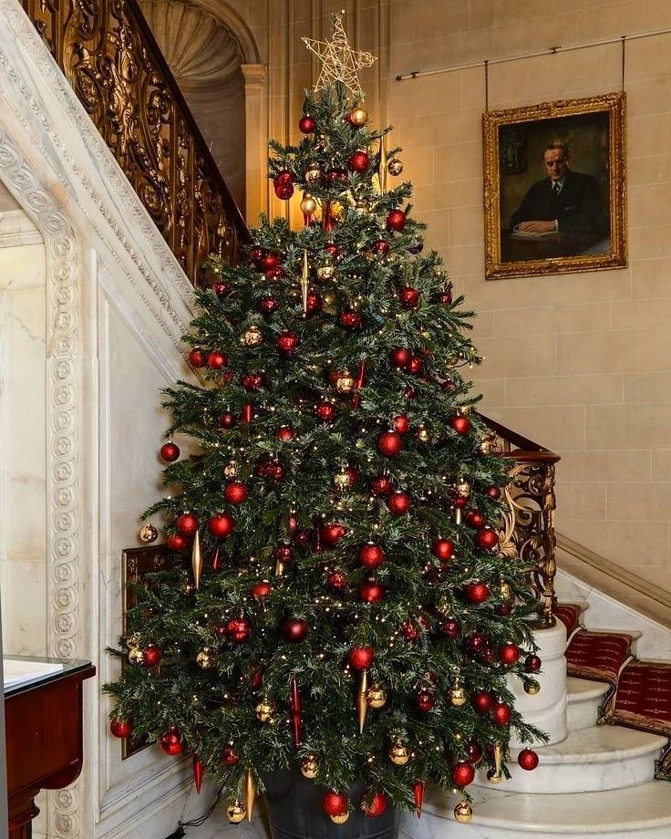 a christmas tree with red and gold ornaments is in the corner of a room next to stairs