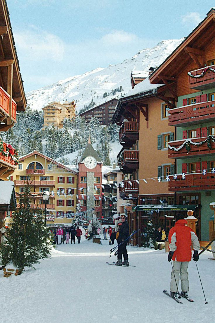 skiers and snowboarders in front of buildings on a ski slope