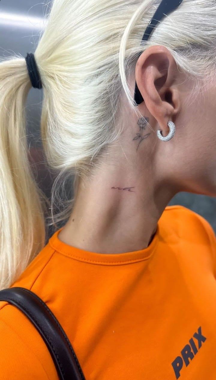 a woman with a tattoo on her neck and behind her ear is looking down at the ground