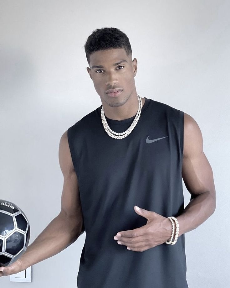 a man holding a soccer ball in his right hand and wearing a necklace on the left