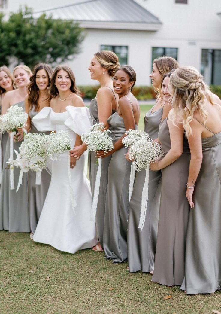 a group of women standing next to each other in front of a house holding bouquets