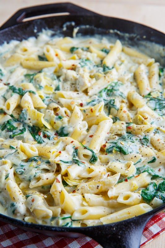 a skillet filled with pasta and spinach on top of a checkered table cloth