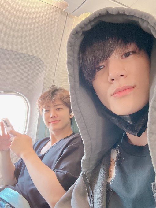 two young men sitting on an airplane looking at their cell phones and taking selfies