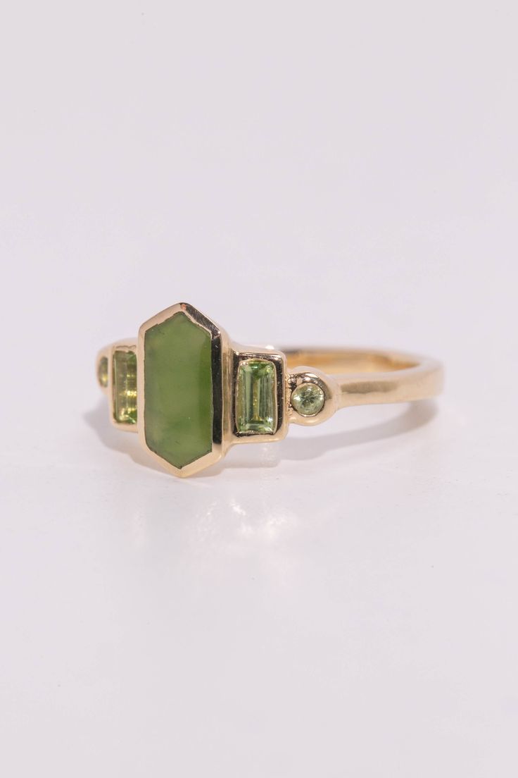 Art deco inspired ring featuring Jade and August's birthstone, peridot. The glowing green centerstone is British Columbia Jade, and it has beautiful depth of color. The jade is inlaid into the elongated hexagon, measuring 9.5mm x 5mm. Light green Arizona peridot are at the sides, and are approximately .30 total carat worth. Millimeter measurement from end to end is 15mm. Your choice of gold color and karat. Band is 1.75mm thick. Please leave a note at checkout with your preferred size. All gems Art Deco Green Emerald Multi-stone Ring, Art Deco Green Jewelry With Bezel Setting, Green Art Deco Jewelry With Bezel Setting, Art Deco Green Ring With Bezel Setting, Art Deco Green Emerald Ring In 14k Gold, Art Deco Emerald Ring In 14k Gold, Art Deco Green Octagon Jewelry, Art Deco Green Jewelry With Accent Stones, Green Octagon Ring With Bezel Setting