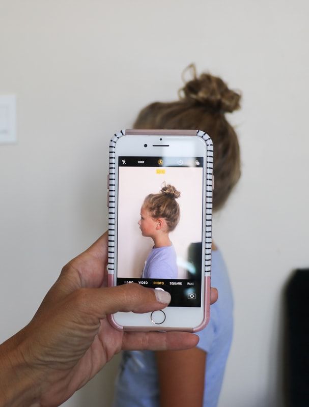 a person holding up a cell phone to take a selfie with her hair styled into a bun