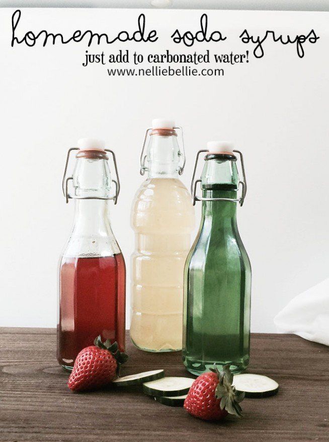 three glass bottles filled with liquid sitting on top of a wooden table next to sliced strawberries