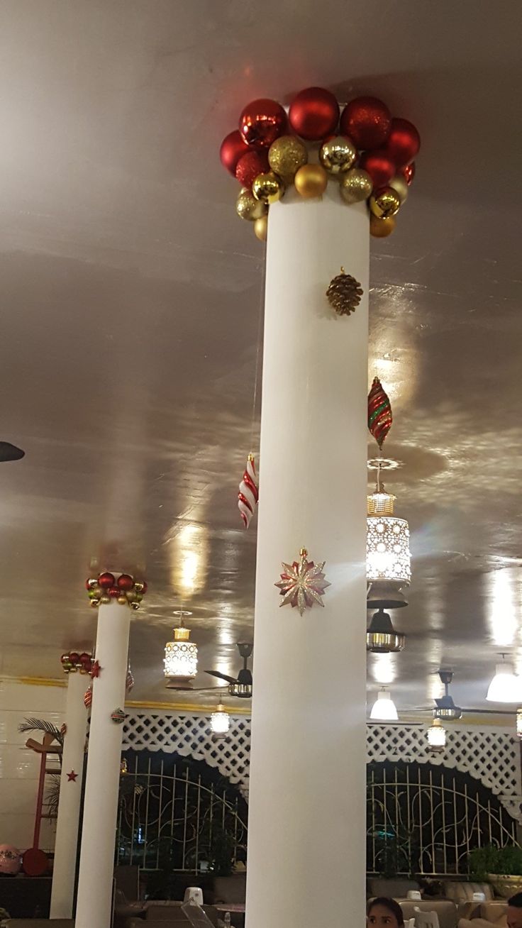 people sitting at tables in a restaurant with red and gold decorations on the pillars above them