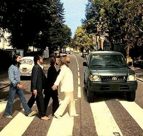 people crossing the street in front of a car on a crosswalk with trees and buildings behind them