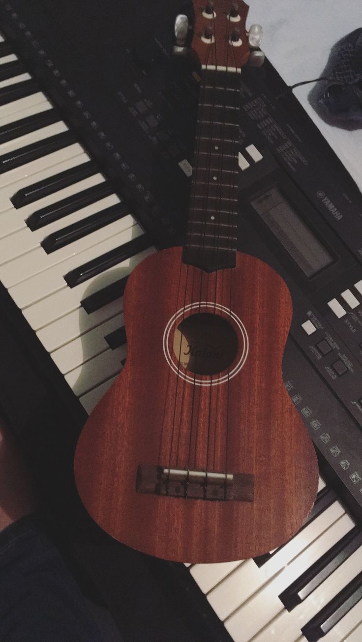 a ukulele sitting on top of a piano keyboard with an instrument in the background