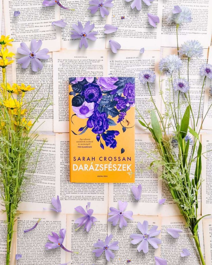 a book sitting on top of an open book next to purple flowers and green leaves