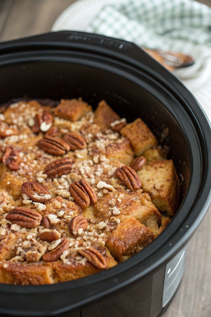 a crock pot filled with bread and pecans on top of a wooden table