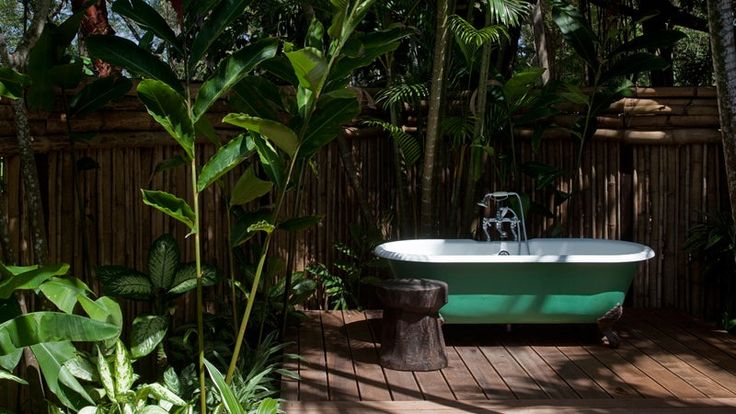 a bath tub sitting on top of a wooden floor next to lush green plants and trees