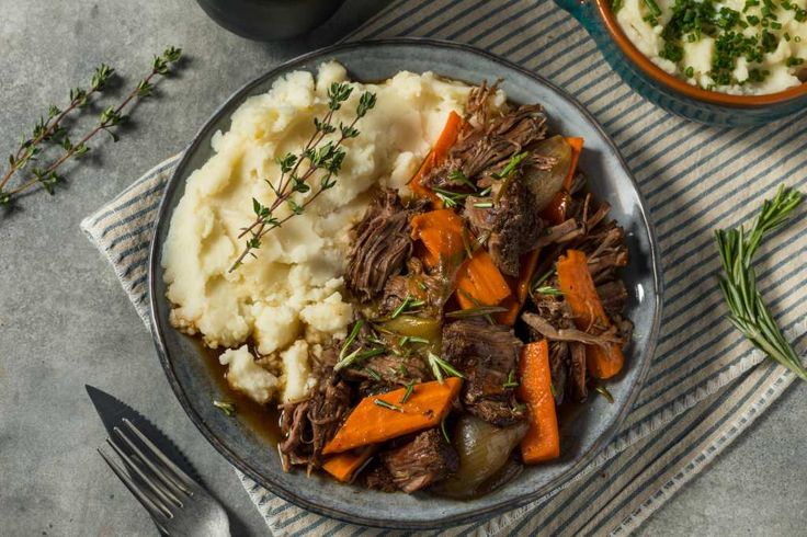 a bowl filled with meat, potatoes and carrots next to a cup of mashed potatoes