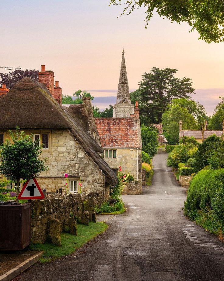 an old country road with thatched roof houses in the distance and trees on either side