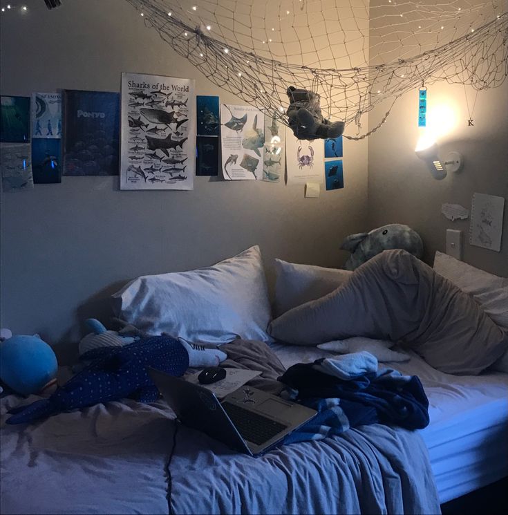 a laptop computer sitting on top of a bed covered in white sheets and blue pillows