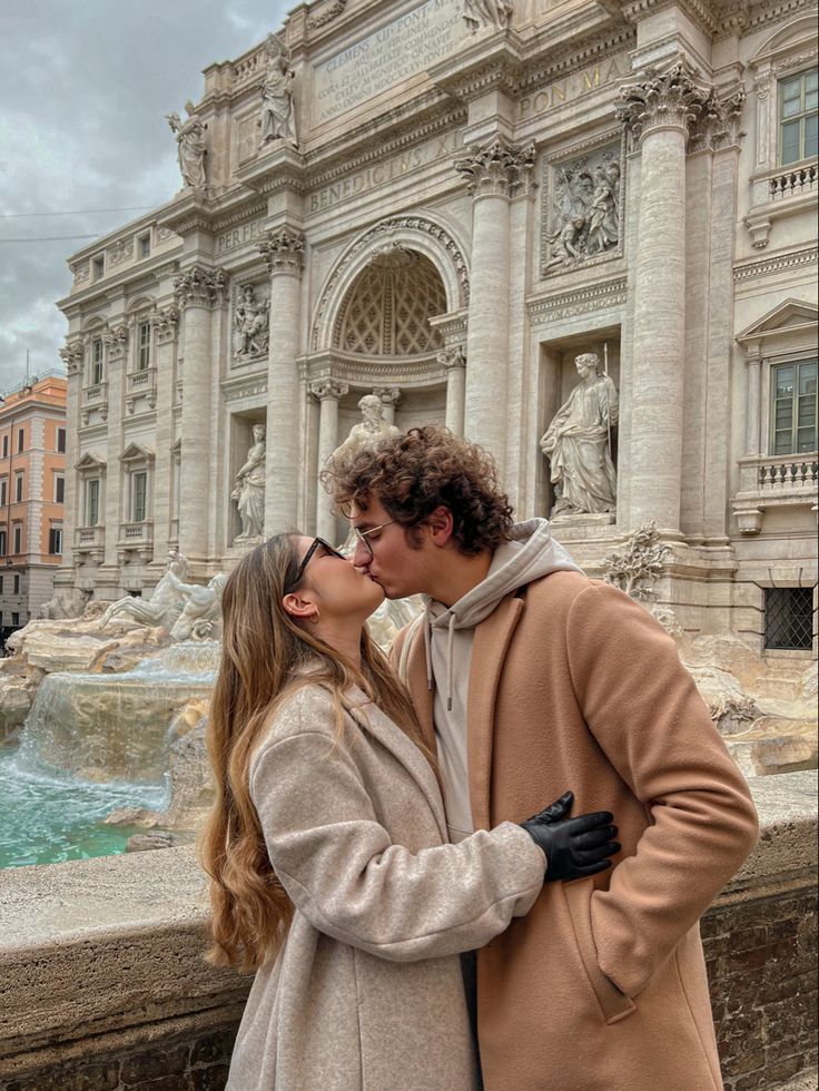 a man and woman kissing in front of a fountain