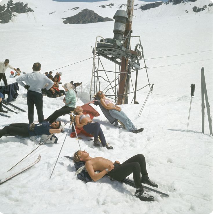 skiers and snowboarders rest in the snow near a ski lift while others look on