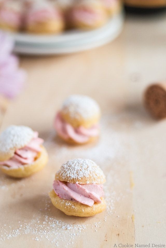 small pastries with pink icing and powdered sugar are on a wooden table