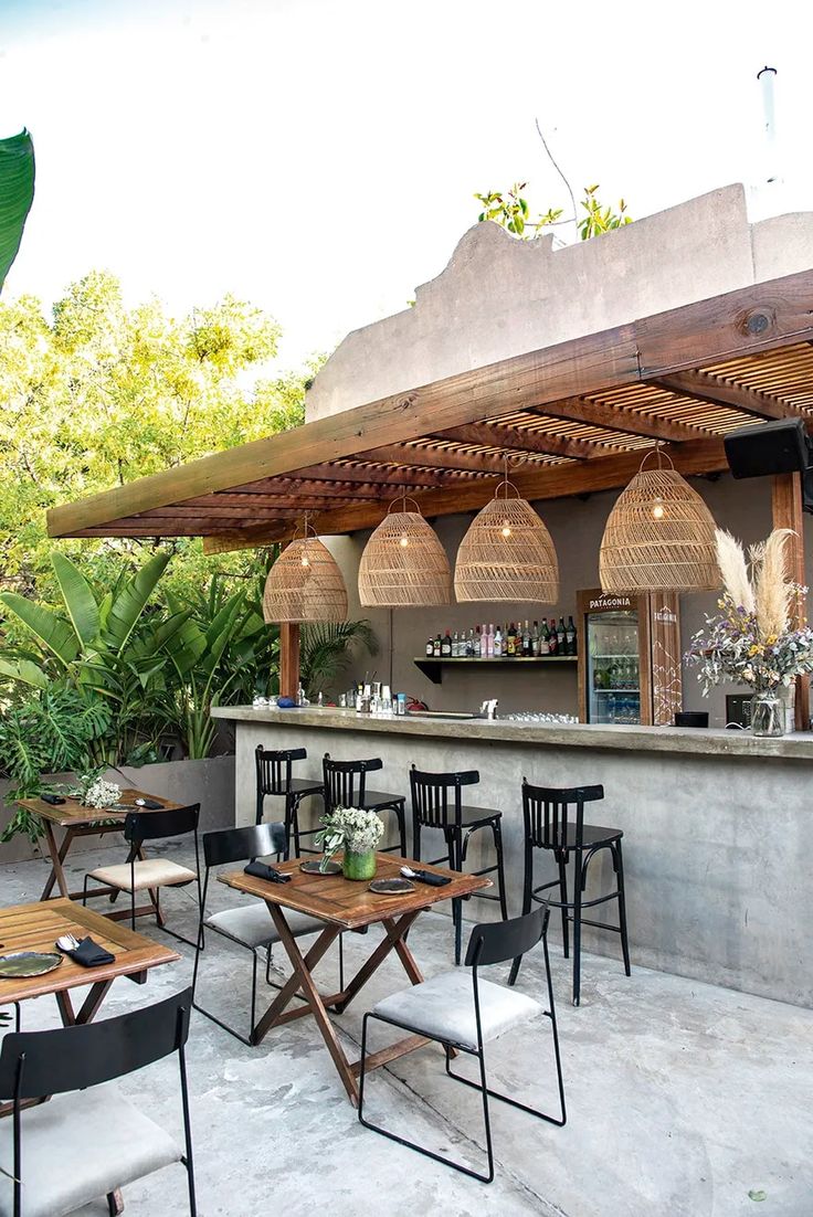 an outdoor bar with tables and chairs under a wooden awning next to some plants