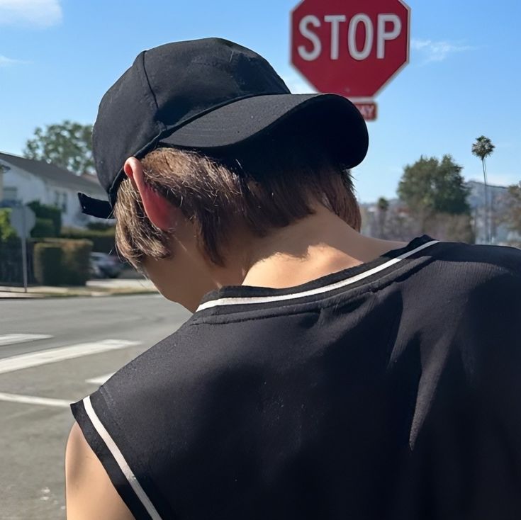 a boy wearing a baseball cap standing in front of a stop sign with his back turned to the camera