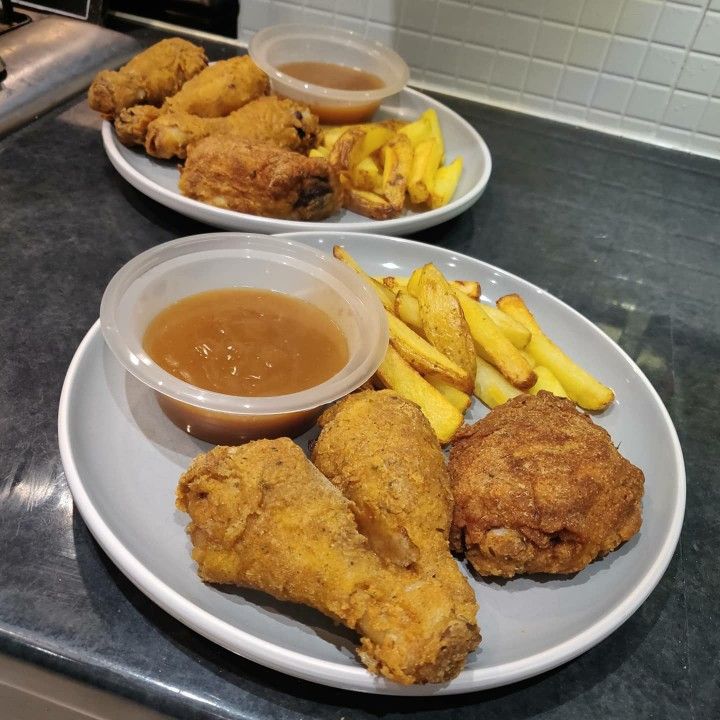 two plates filled with fried chicken, fries and gravy on top of a counter