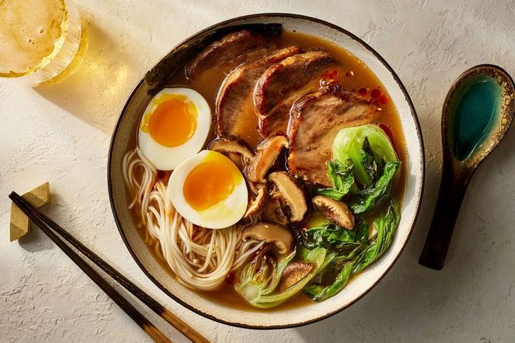 a bowl of ramen with meat, mushrooms and egg on the side next to chopsticks