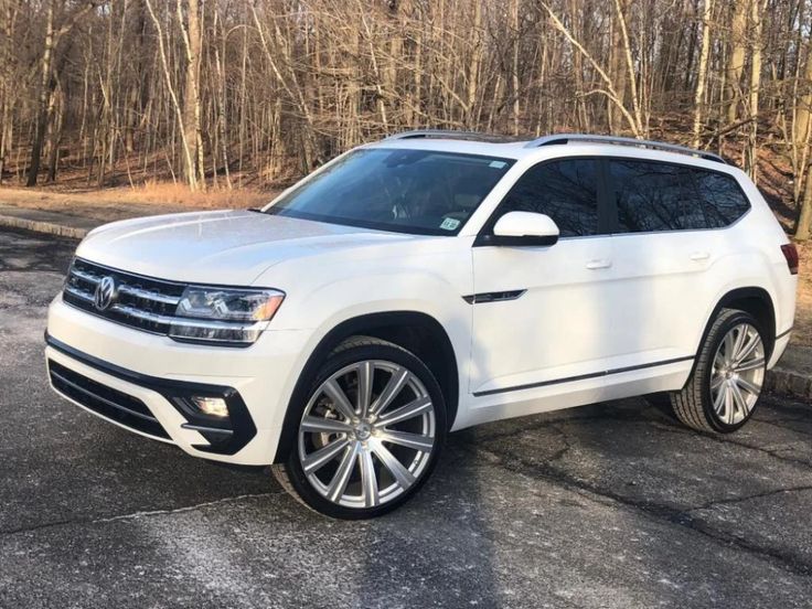 a white volkswagen suv parked in front of some trees