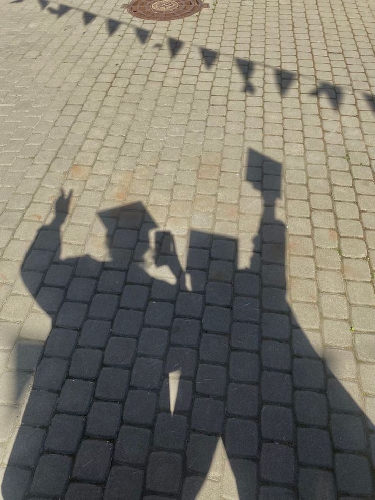 the shadow of two people standing next to each other on a brick walkway with flags in the background