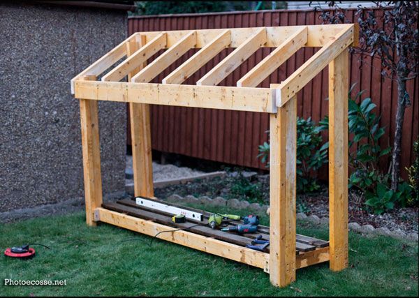 a wooden structure sitting in the grass next to a building with tools on top of it