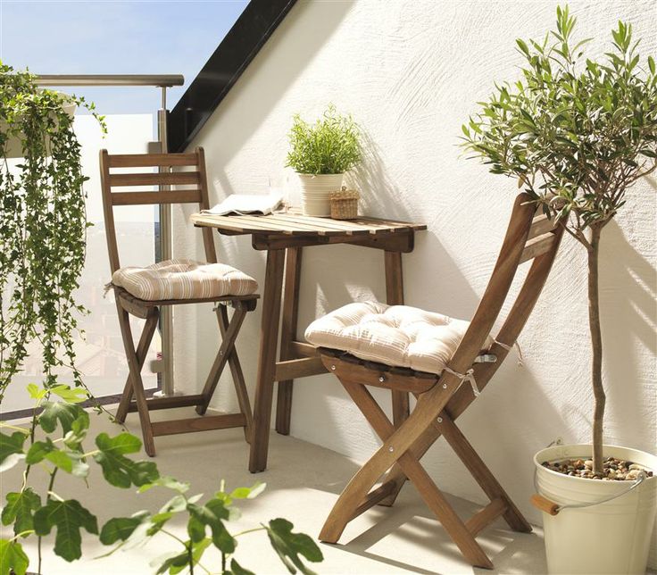 two wooden chairs sitting on top of a balcony next to a small table and chair