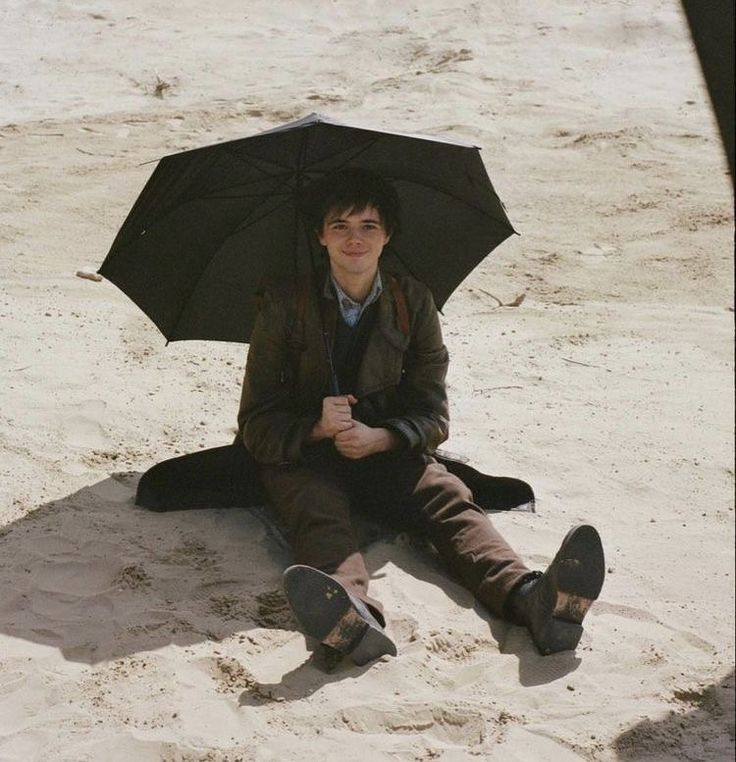 a man sitting in the sand with an umbrella