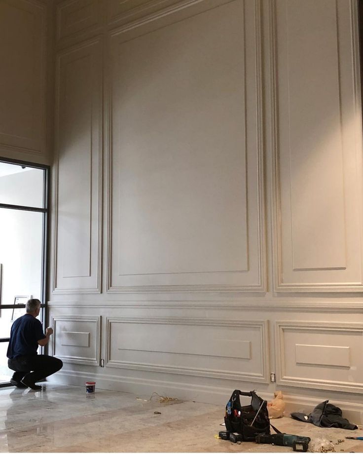 a man kneeling down on the floor in front of a wall with white paneling