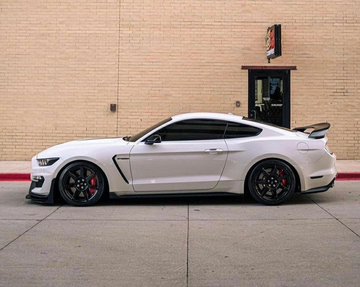 a white mustang parked in front of a brick building