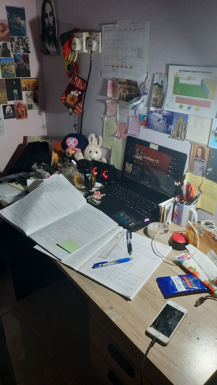 an open book sitting on top of a wooden desk next to a laptop and phone