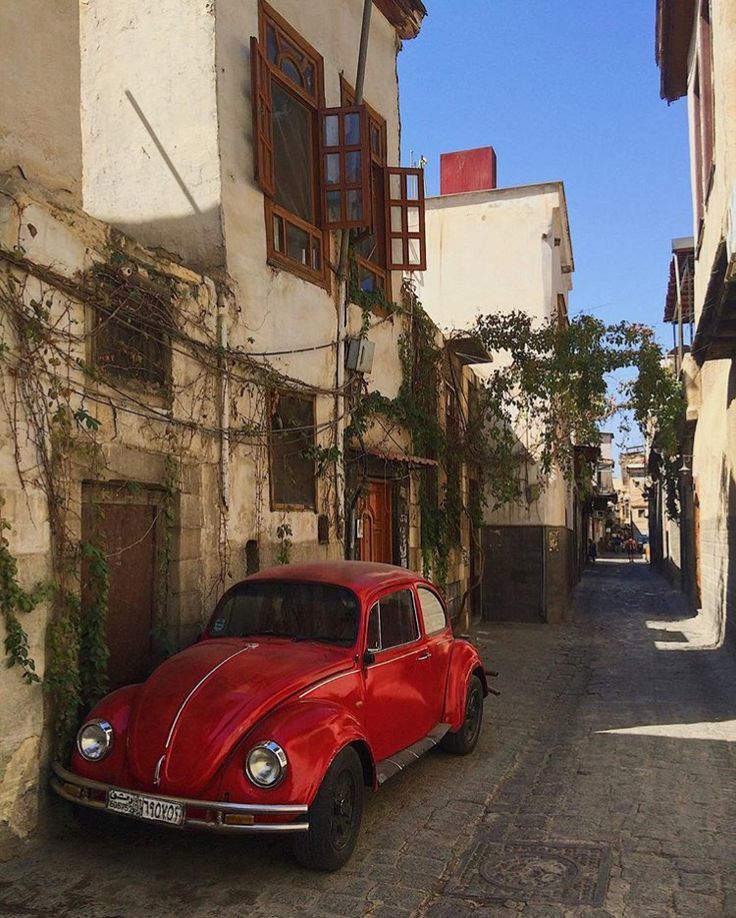 an old red car parked on the side of a street next to tall white buildings