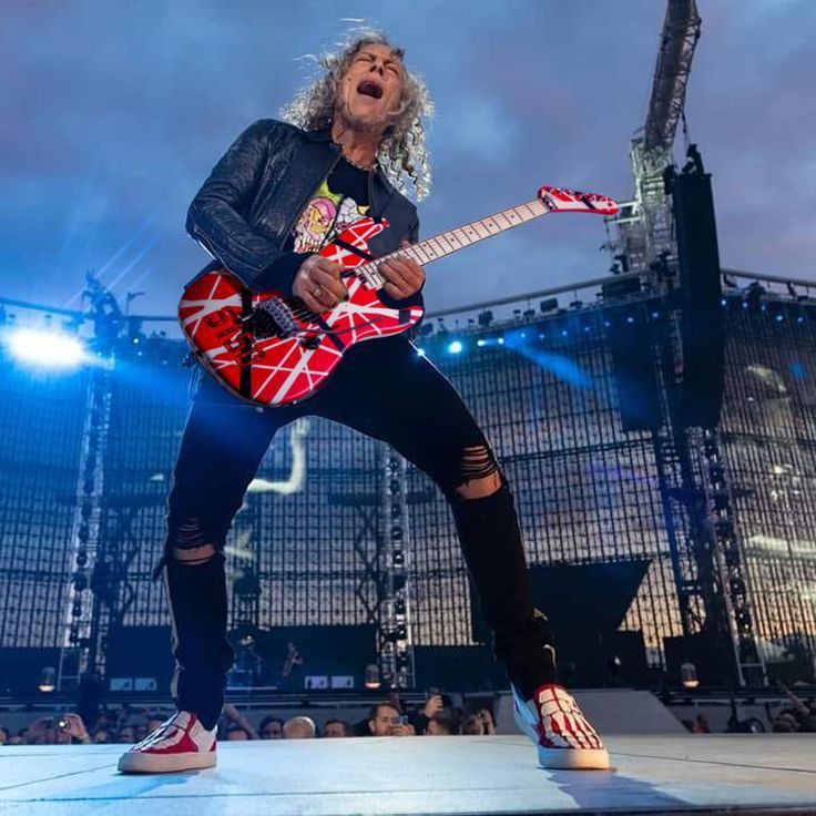 a man with long hair playing an electric guitar in front of a crowd at a concert