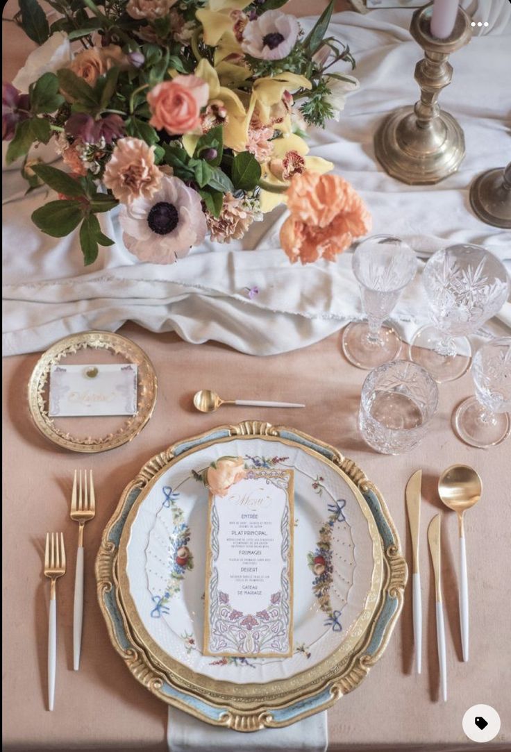 the table is set with gold and white plates, silverware, and floral centerpieces