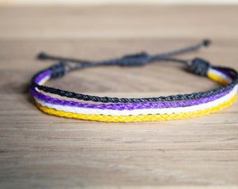 a yellow, purple and white bracelet on a wooden table with black string attached to it