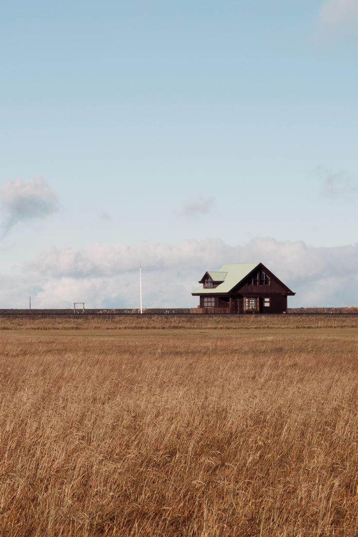 an old house in the middle of a field with tall brown grass and blue sky