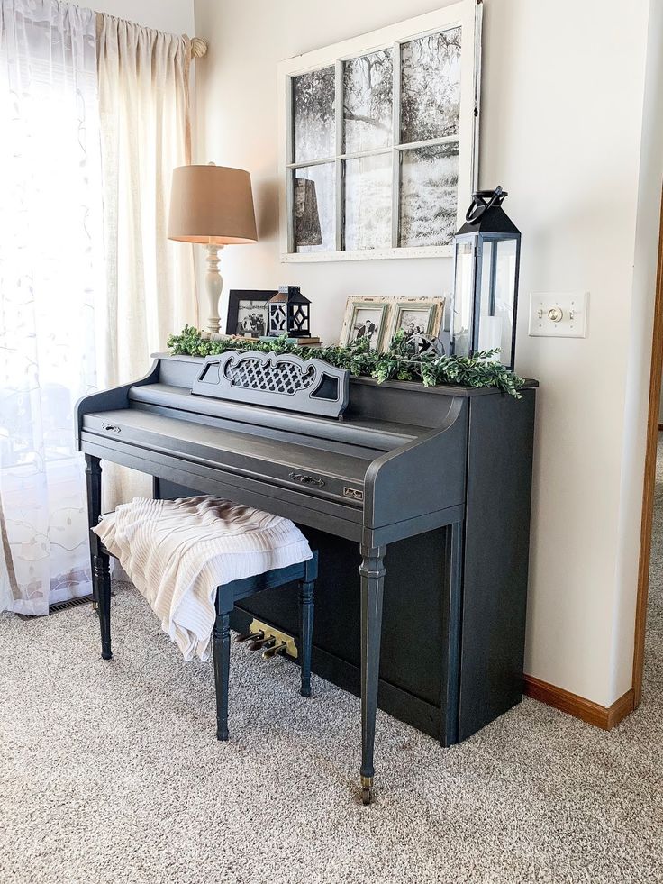 a black piano sitting in front of a window next to a lamp and pictures on the wall