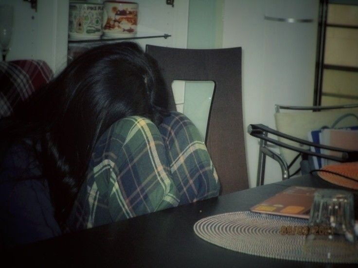 a woman sitting at a table with her head on the back of a chair and looking down